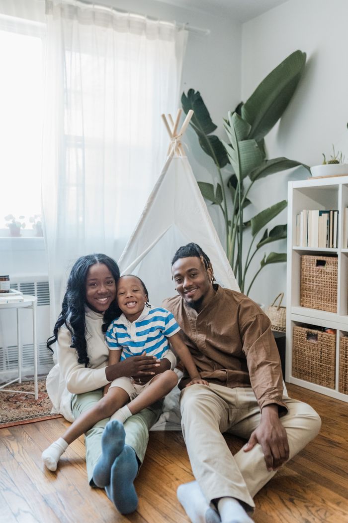 Smiling family sitting together inside a cozy living room with teepee and plants.