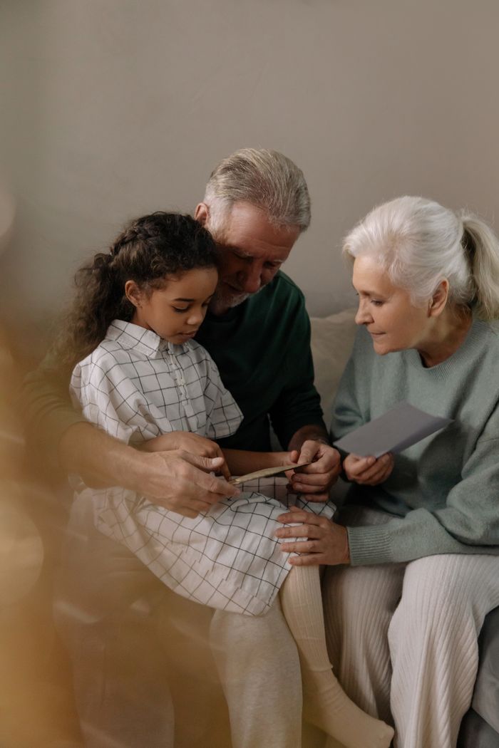 Grandparents sharing a heartfelt moment reading with their granddaughter indoors.